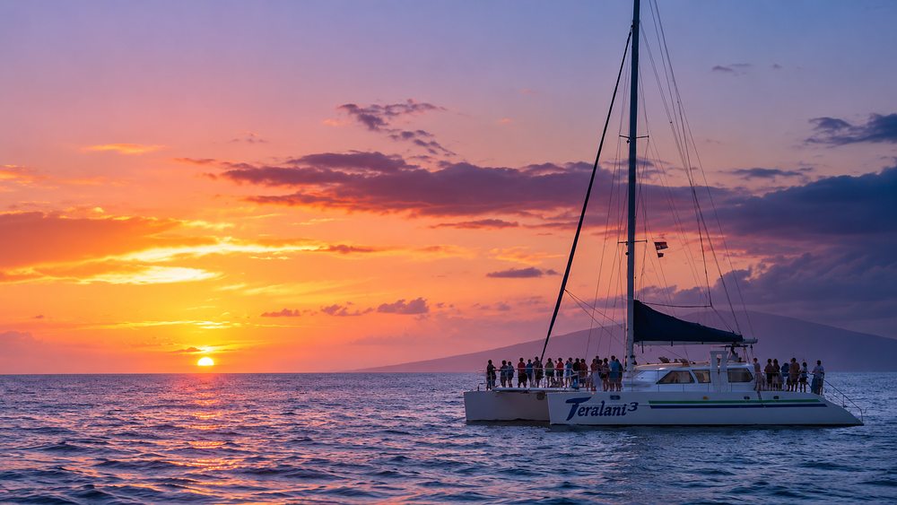 A sailing catamaran carrying passengers on deck at sunset