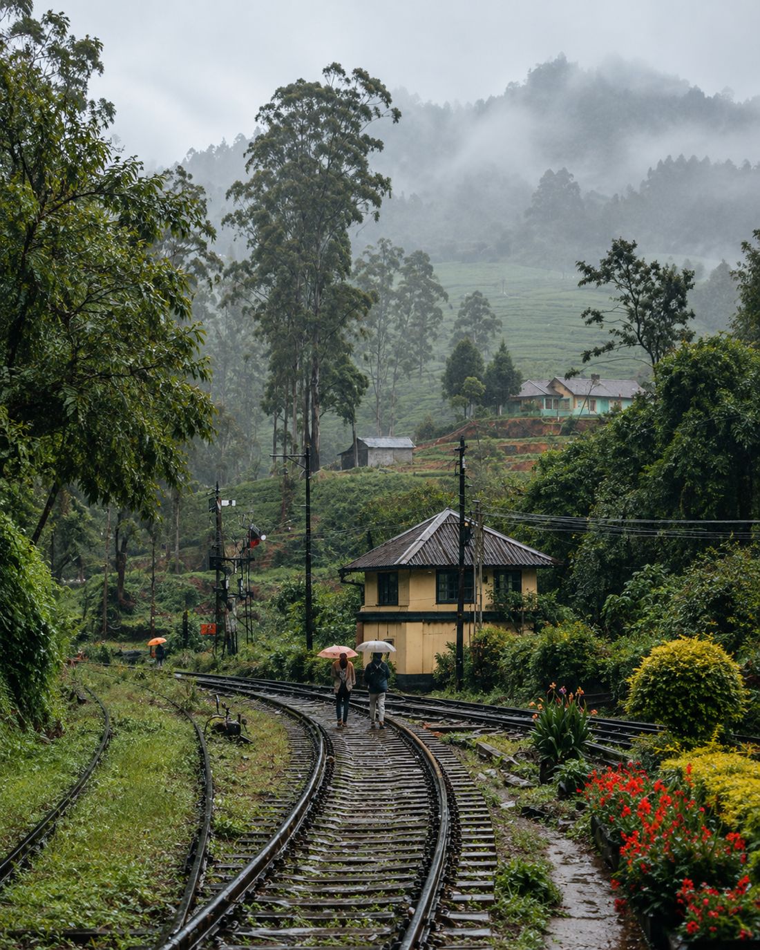 Two people with umbrellas on the tracks beside a signal cabin in the misty hills
