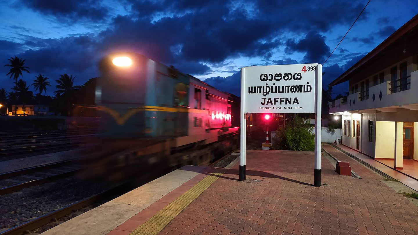 A night train passing the Jaffna station sign at dusk, Sri Lanka