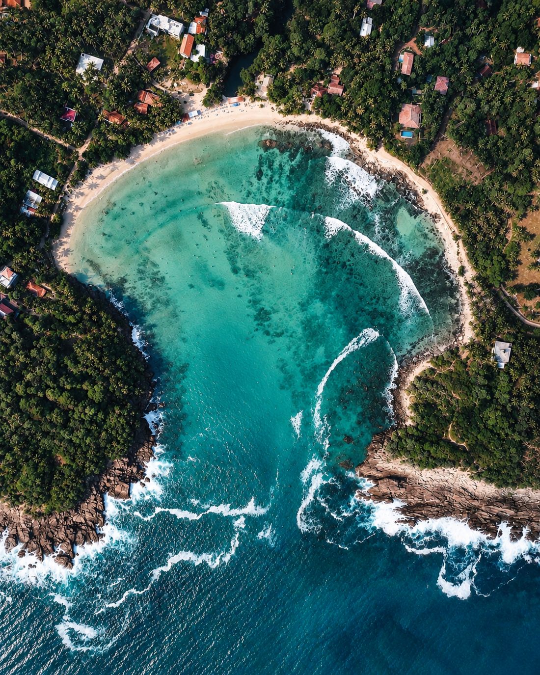 A horseshoe surf bay from above, waves wrapping around the reef