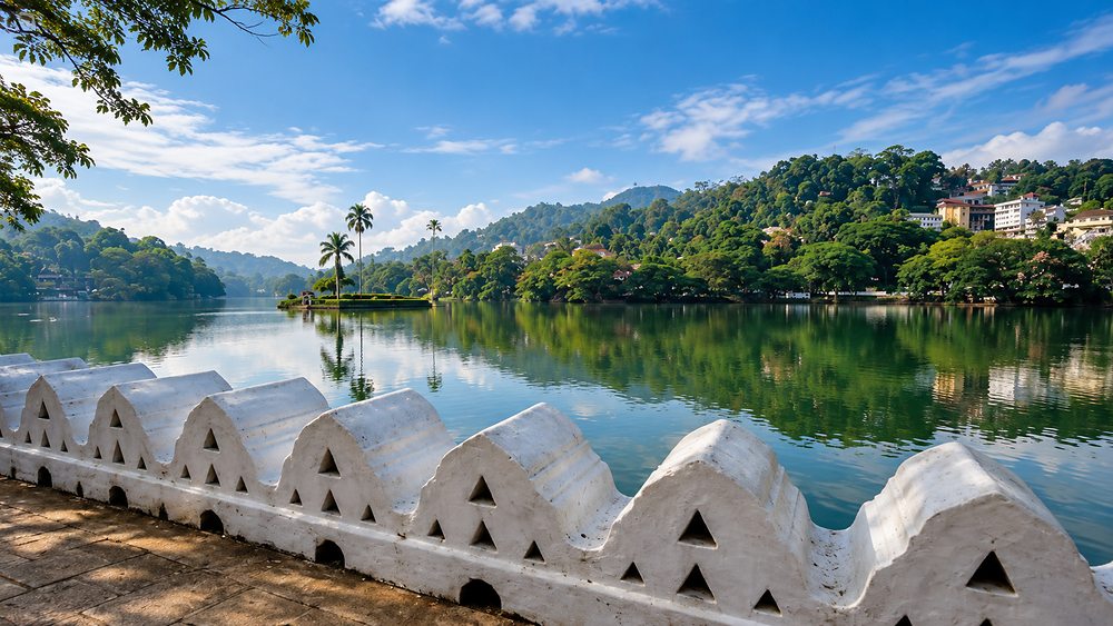 Kandy Lake seen over the temple's white parapet wall, wooded hills beyond, Kandy, Sri Lanka
